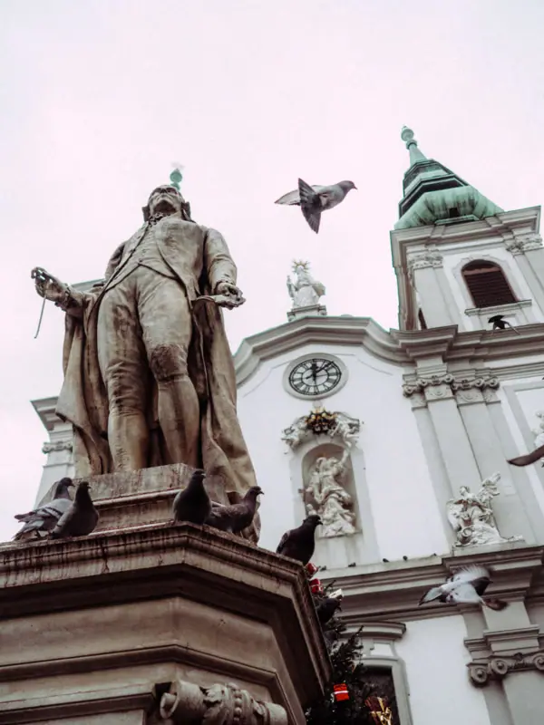 Haydn statue, Vienna A statue of a man with flying doves, set outdoors against a clear sky.