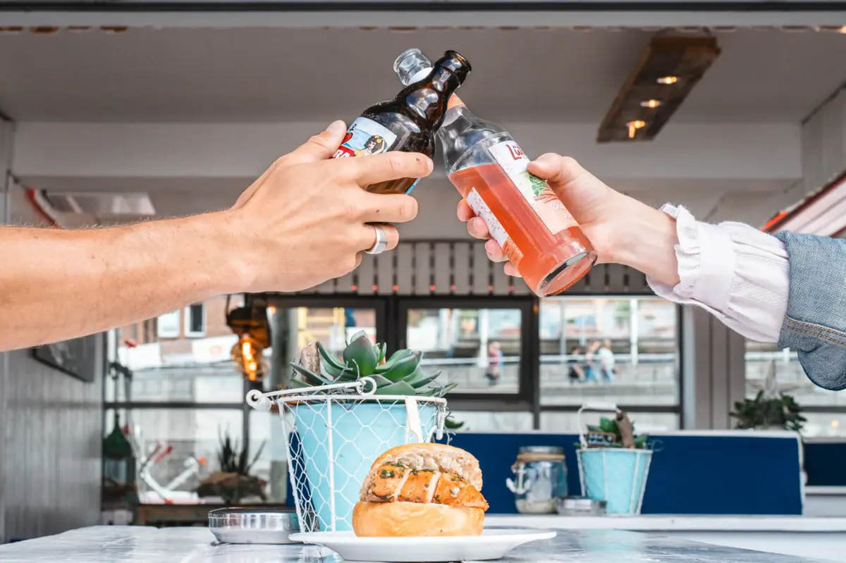 Two hands clink bottles together at a table.