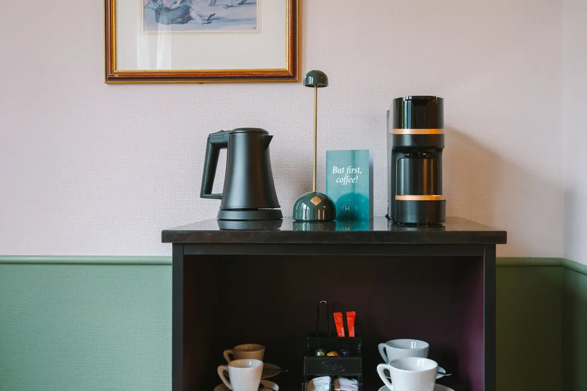 Coffee machine, kettle and cups on a shelf on one wall.