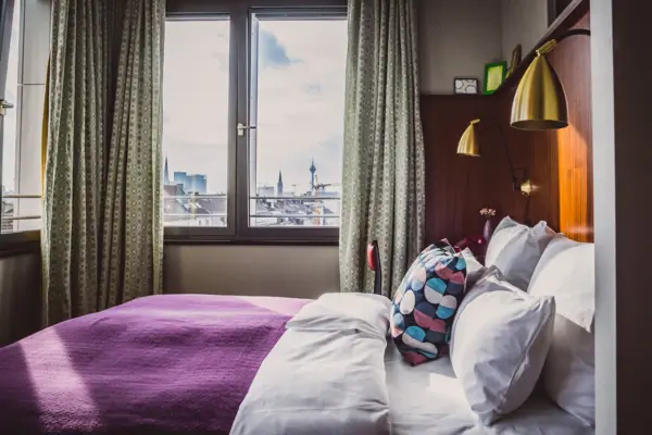 A bed with pillows and a purple blanket in a room with a window.