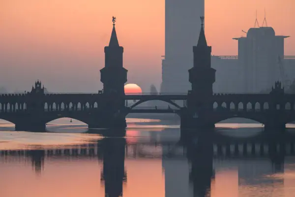 Berlin Panorama Oberbaumbrücke Sunrise Silhouette of the Oberbaumbrücke in Berlin at sunrise, with the towers and the reddish sun reflected in the calm waters of the Spree.