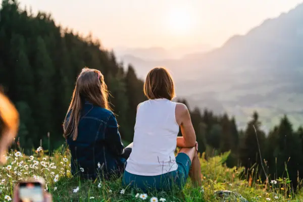 Two women sit on a hill and watch the sunset.