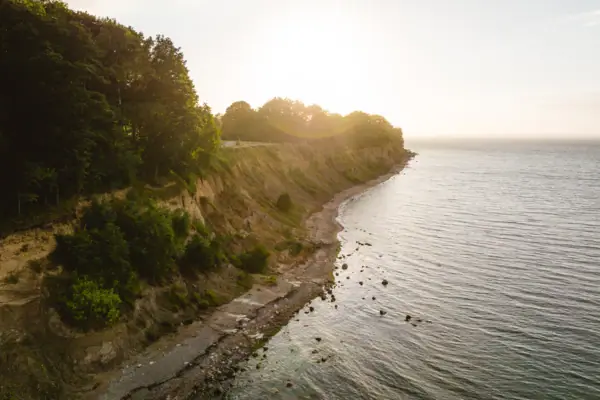 The Brodten shore with a rocky cliff and trees on the water's edge.