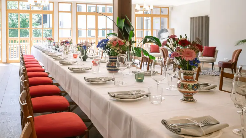 A long table with white tablecloths and red chairs.