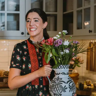 Woman holding a vase of flowers and smiling.