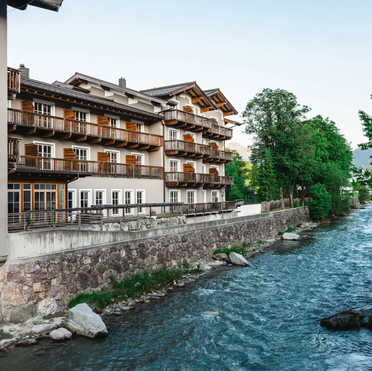 HERNI Kitzbühel A river with a building and trees.