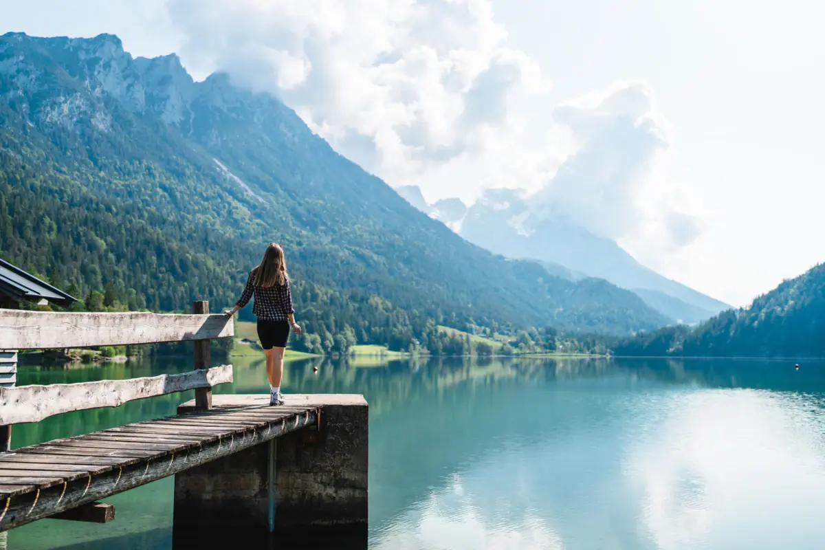 Lake with jetty and person in front of a mountain backdrop