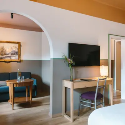 A suite at the HENRI Garmisch-Partenkirchen with a separate living and sleeping area, a desk and a TV on the wall,