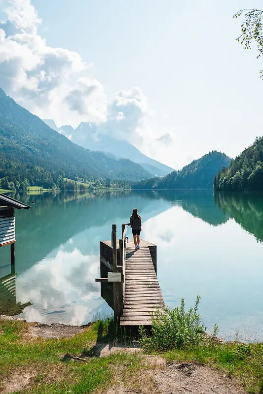 A woman walks on a footbridge across a lake.