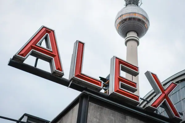 HENRI Berlin Alexanderplatz A sign with a tall tower in the background.