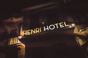 The bright, golden-yellow ‘HENRI HOTEL’ neon sign on the historic exterior façade of the hotel in Berlin at night.