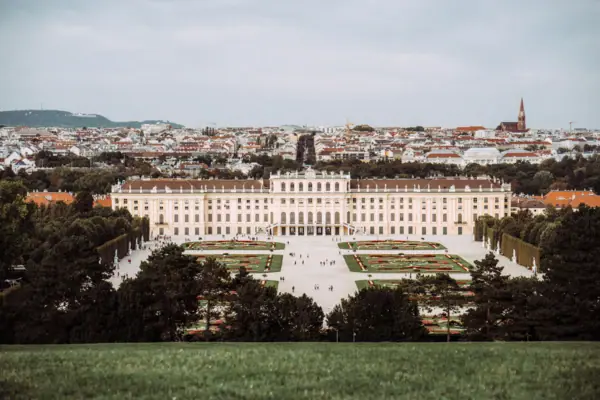 Large building with a courtyard and garden, surrounded by trees and grass under a partly cloudy sky.