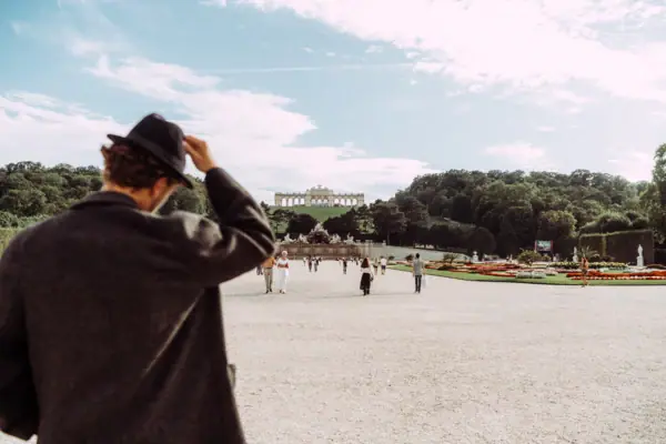 A man in a hat looks down a path leading to Schönbrunn Palace in Vienna.