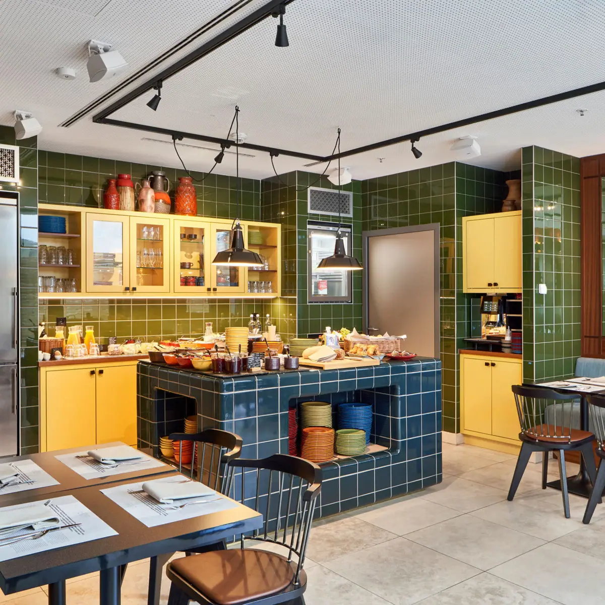 A restaurant with green tiles and yellow cupboards.