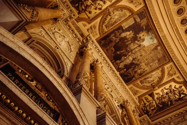 Burgtheater, Vienna A ceiling featuring columns and paintings, symmetrically arranged and elaborately decorated.