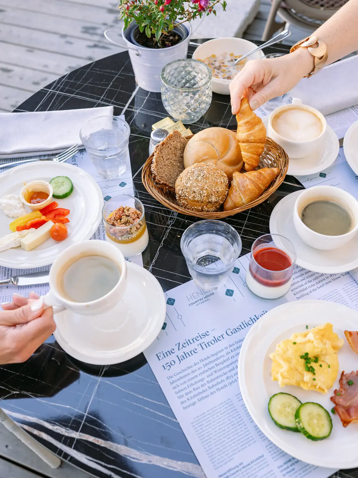 A person is holding a croissant and a bowl of food on a table.