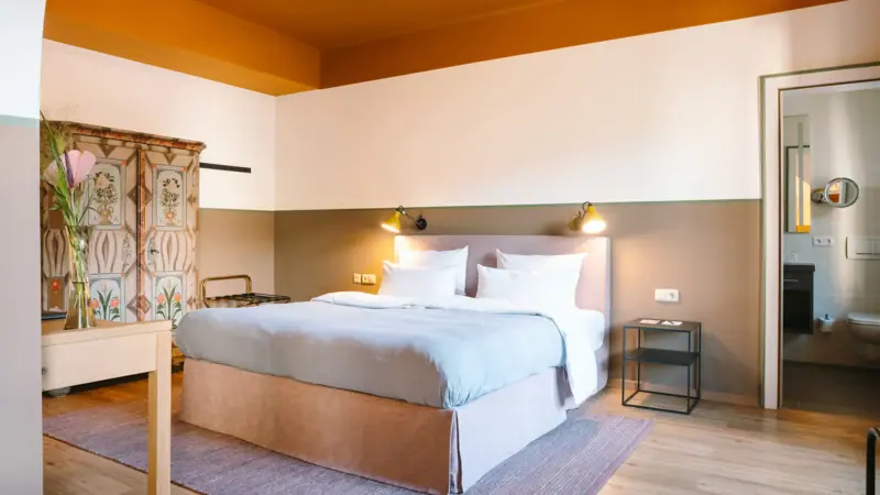 A hotel room at the HENRI Hotel Garmisch-Partenkirchen with a cosy bed and an old wardrobe.