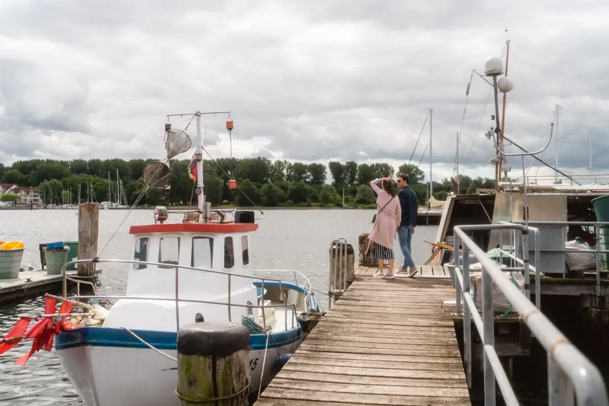 A man and a woman stand on a jetty next to a boat in Travemünde harbour.