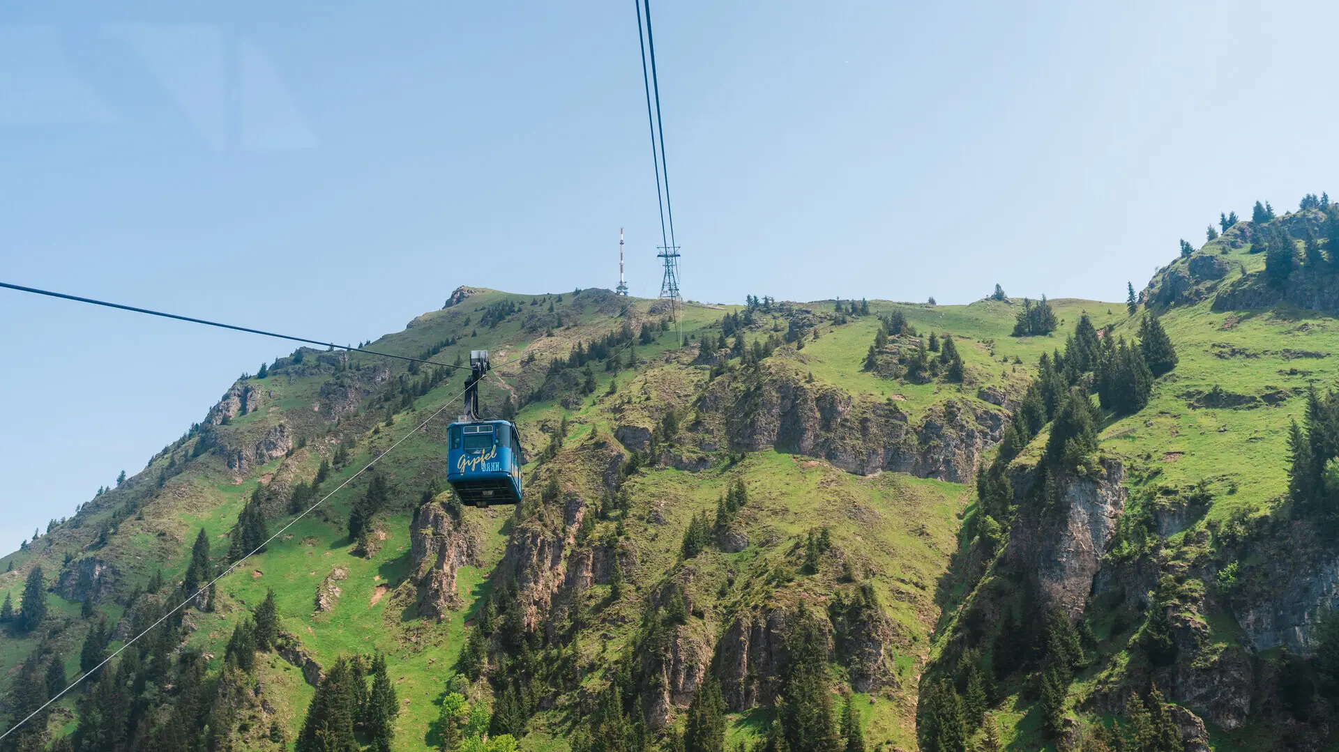 A cable car is travelling up a mountain against a blue sky.