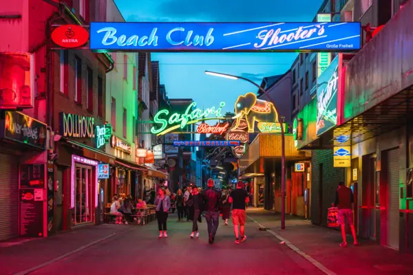 A group of people walk along a street with illuminated neon signs.