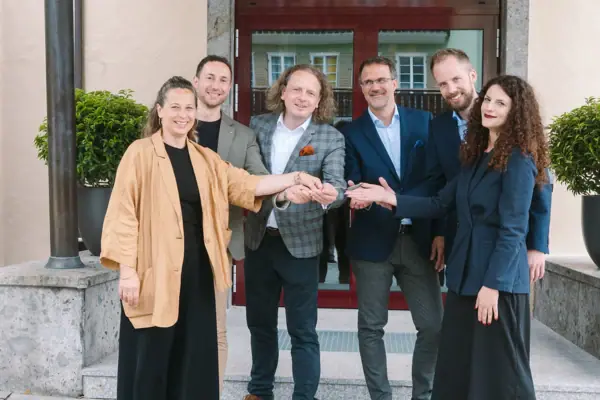 A group of people smiling and standing in front of a building, wearing coats and jeans.