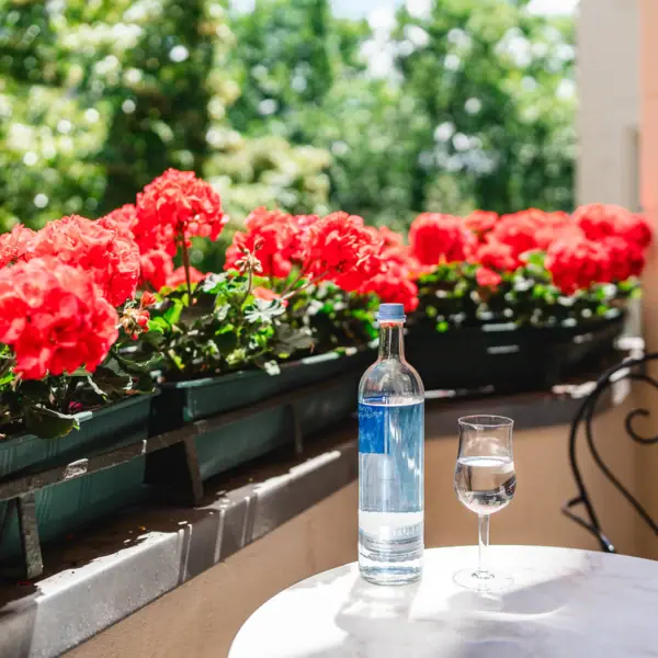 A bottle and a glass of water on a table with red flowers.