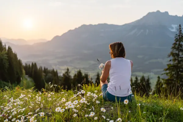 A woman sits on a hill with flowers.