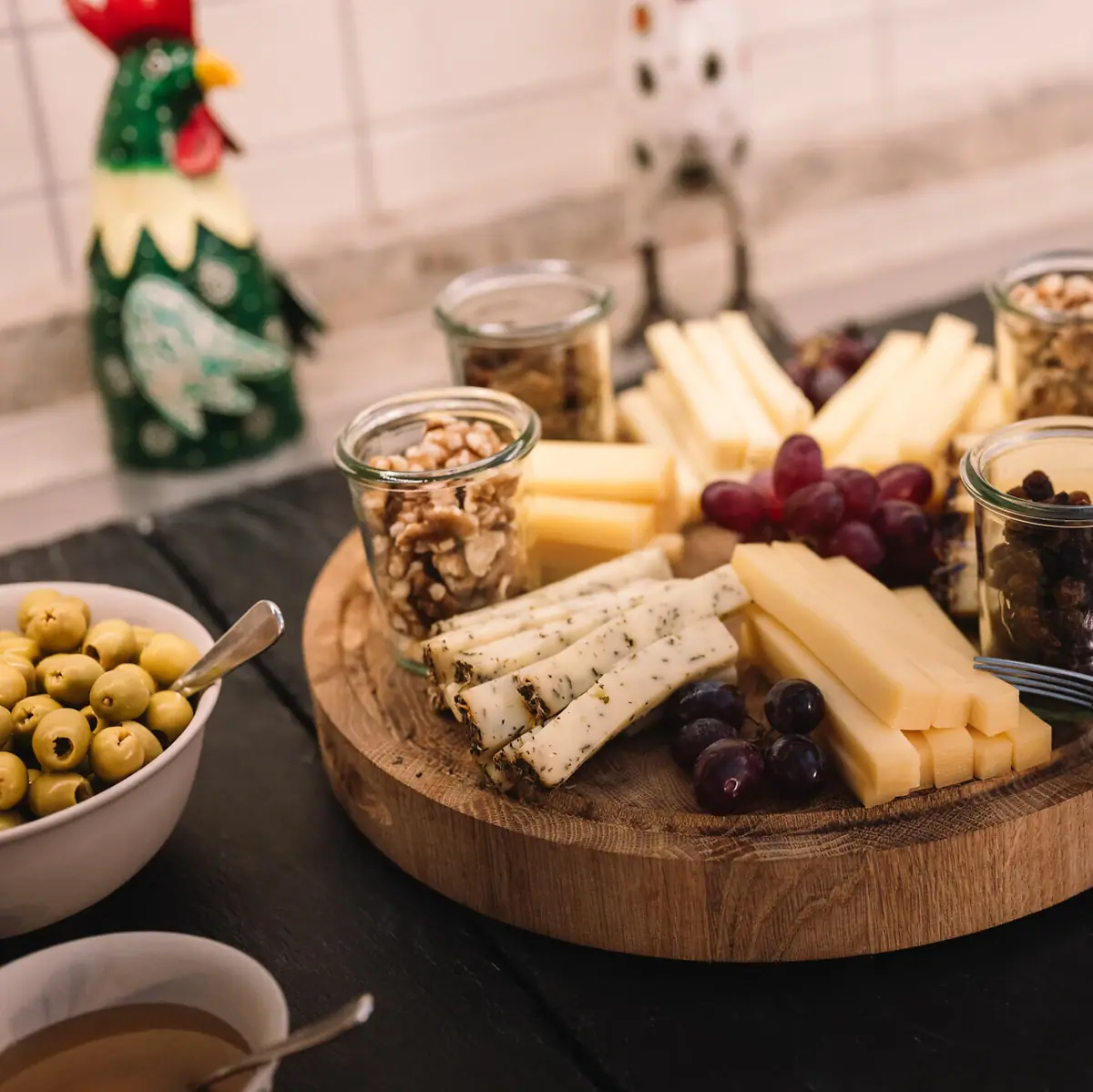 A wooden board on a buffet with cheese, grapes and nuts.