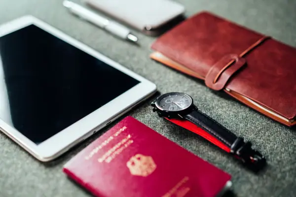 A tablet and a passport, alongside a pen and a watch.