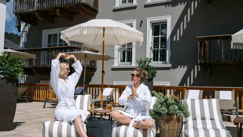 Two women in bathrobes sit on a terrace.