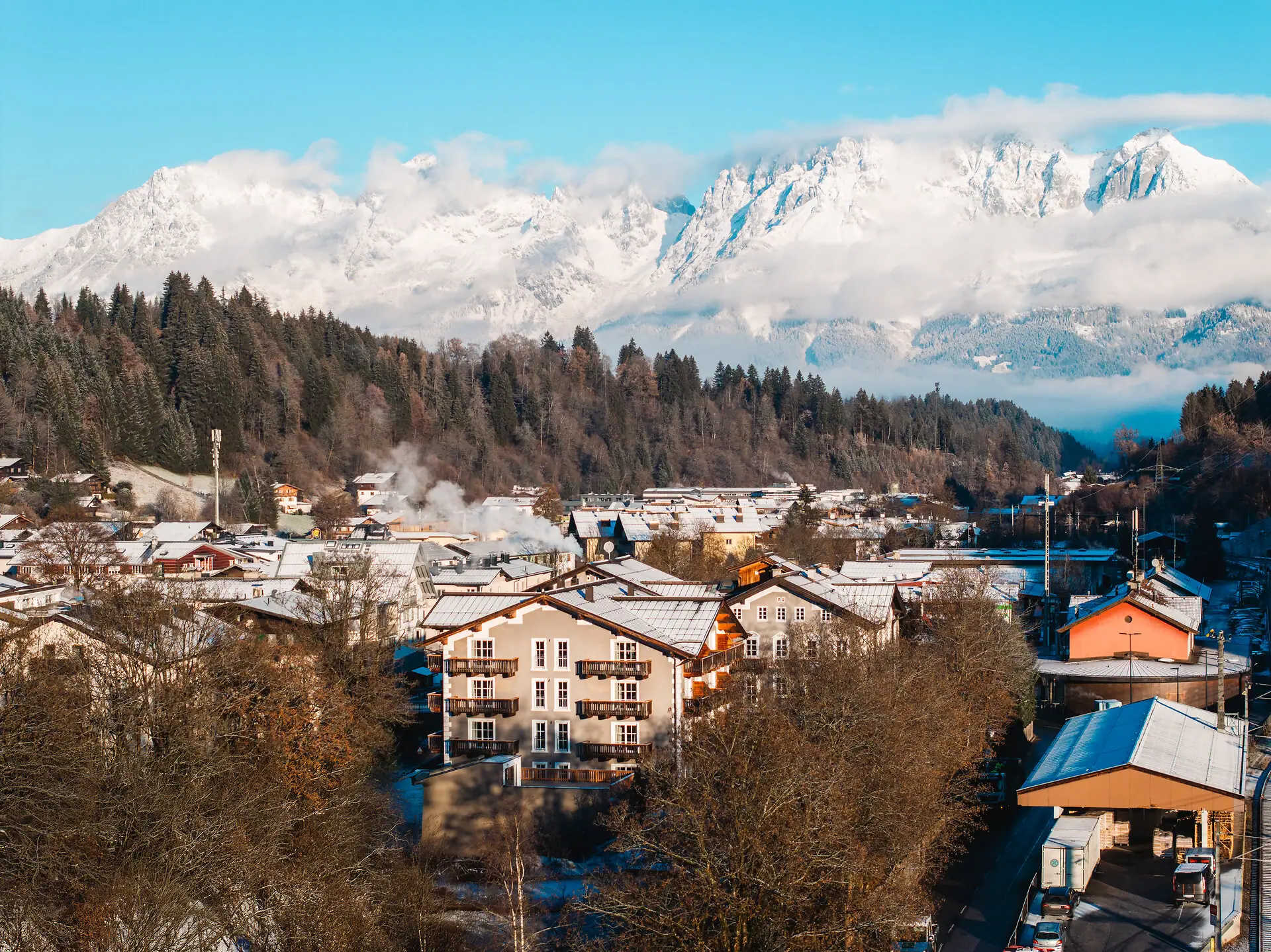 HENRI Kitzbühel drone view A mountain village with snow-capped mountains in the background.
