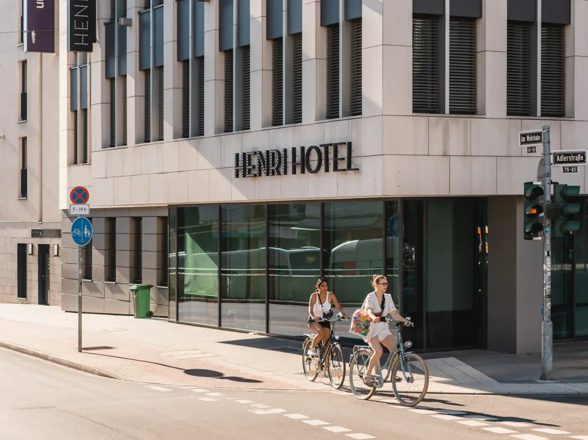 A group of people riding bicycles on a street in front of a hotel.