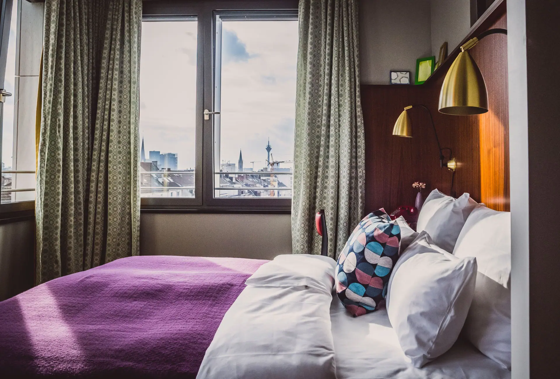Bed with pillow and purple blanket in a room with a window.