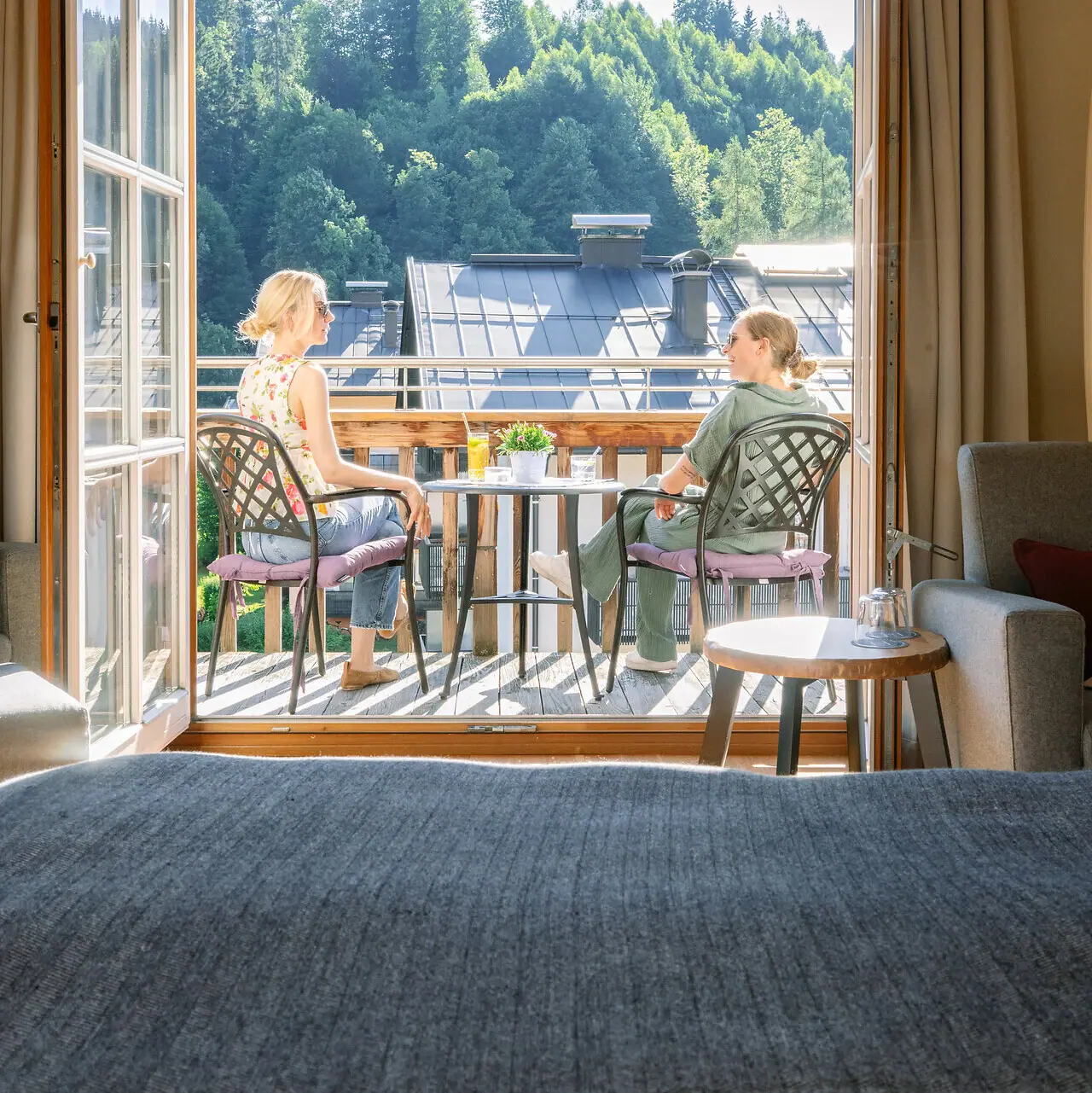 Two women sit on a balcony and look out of a window.