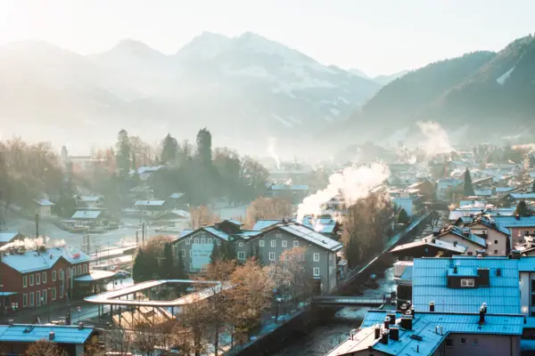 Snow-covered roofs of a city with mountains in the background.