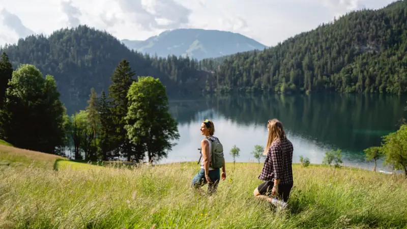 Two people are standing in a grassy field by a lake.