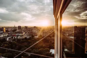 View of a city through a window with clouds and buildings in the sky.