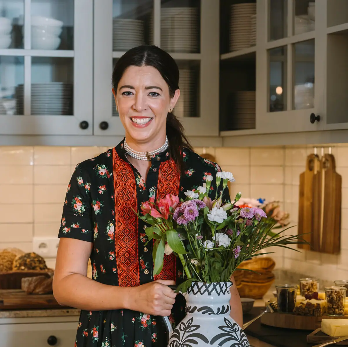 Hotel manager Susanne with a bouquet of flowers in the hotel kitchen, with various dishes in the background.