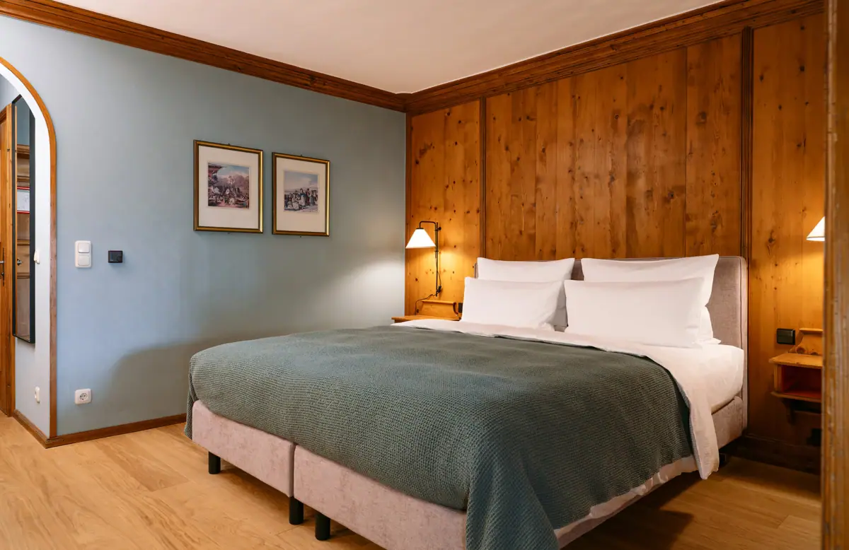 Rooms at the HENRI in Garmisch-Partenkirchen A bed with a wood-panelled wall and a lamp.