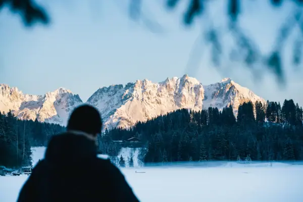 Kitzbühel Alps A person is standing in front of a snow-capped mountain.