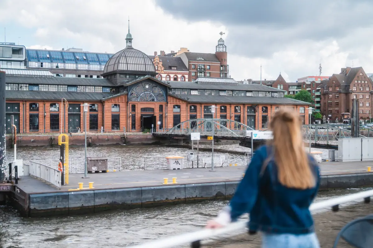 A woman is standing on a ship, looking at a building.