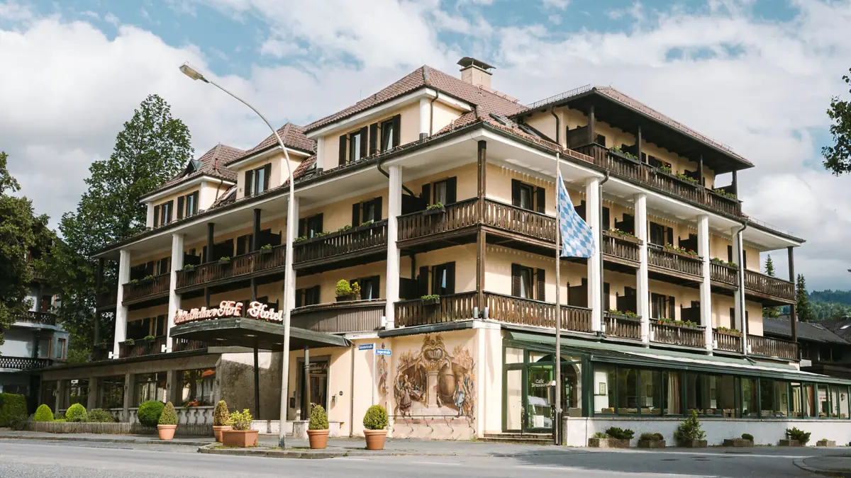 Exterior view of the HENRI Garmisch-Partenkirchen with green trees and a blue sky. 