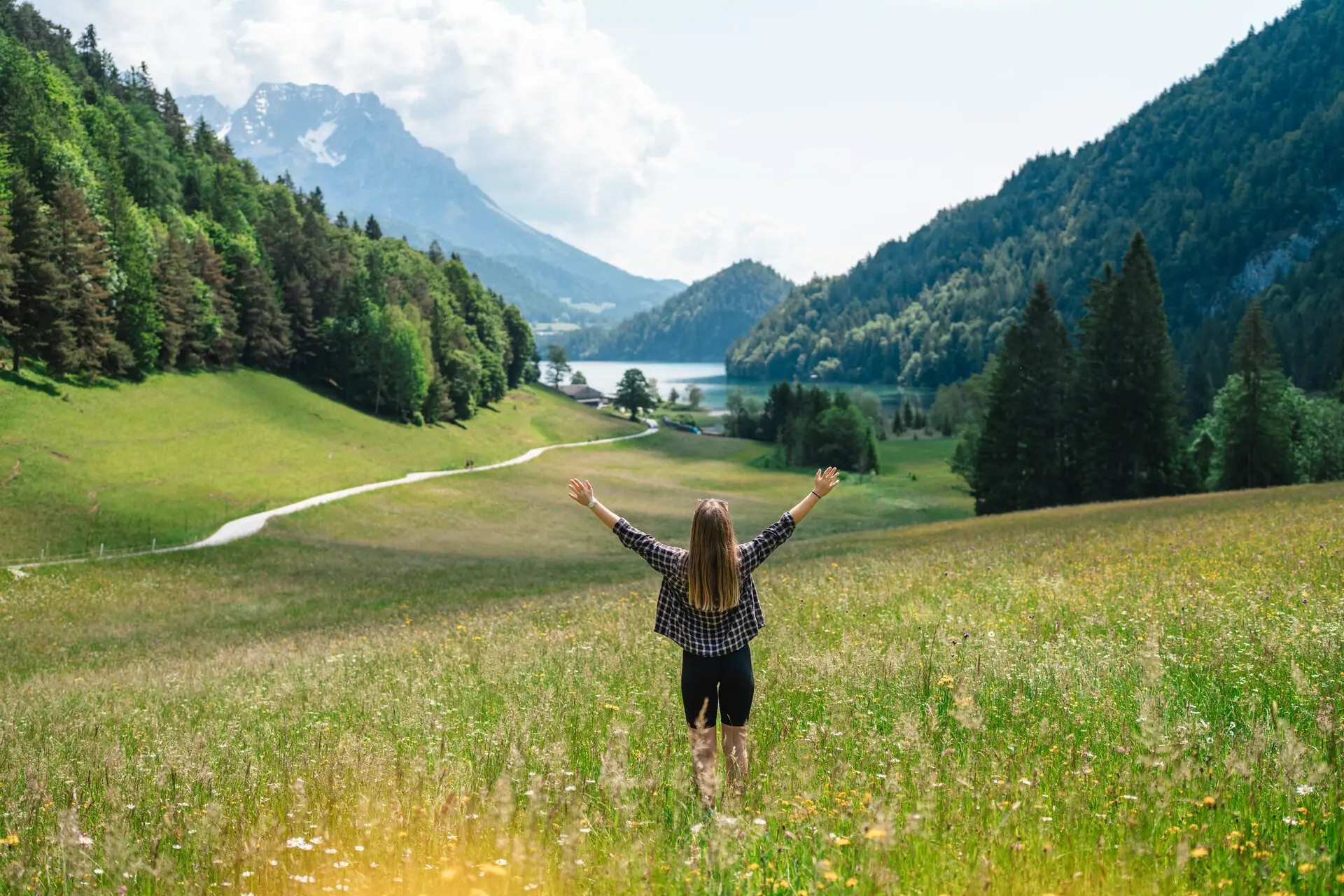 A woman stands in a field with her arms raised.