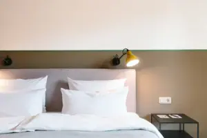 A bed with white pillows in front of a two-coloured wall in the HENRI Hotel Garmisch-Partenkirchen.