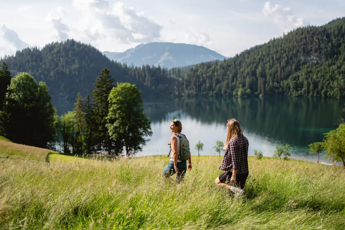 Two people are standing in a grassy field by a lake.