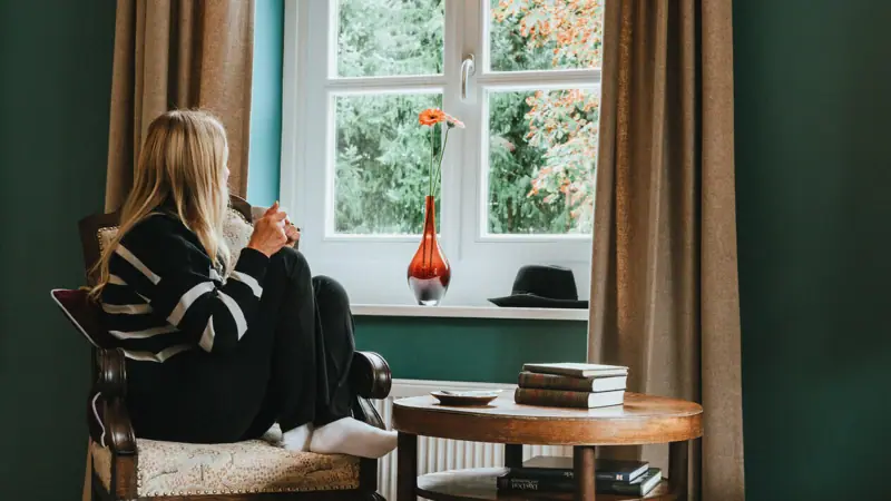 A woman is sitting on a chair and looking out of the window.