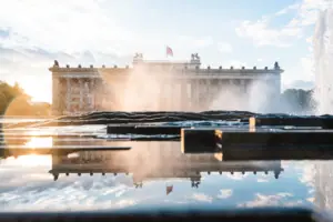 The Altes Museum in Berlin at sunset, seen through the water fountains of a fountain with a reflection in the foreground.
