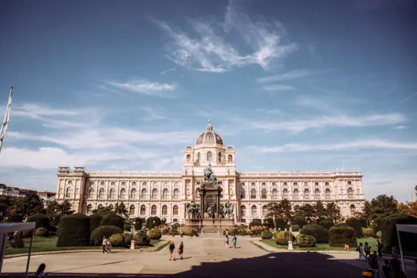 Large building with a statue in front of it, surrounded by trees and sky in the background.