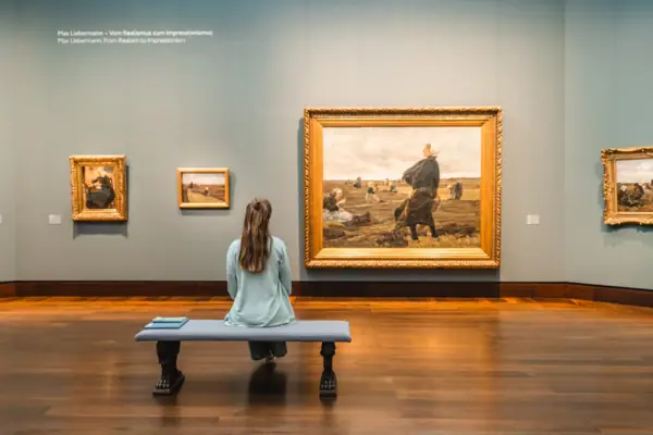 A woman sits on a bench and looks at a painting in an art gallery.