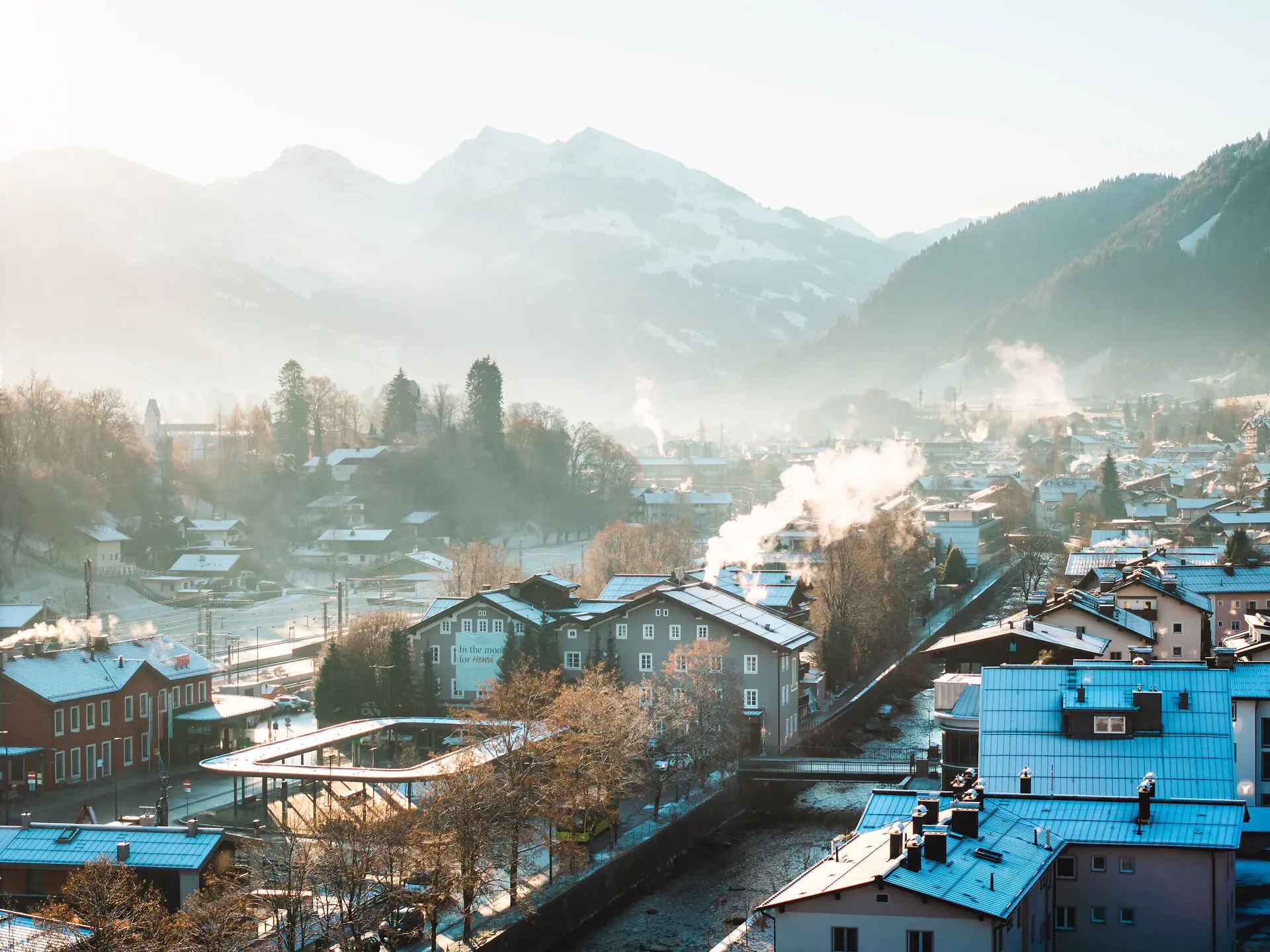 Snow-covered roofs of a city with mountains in the background.
